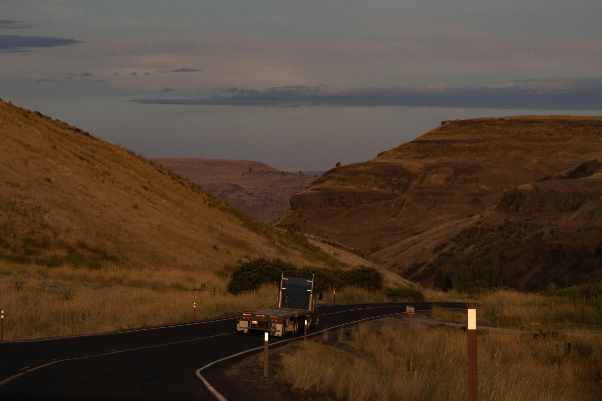 Flatbed truck climbing a winding road through hills at sunset